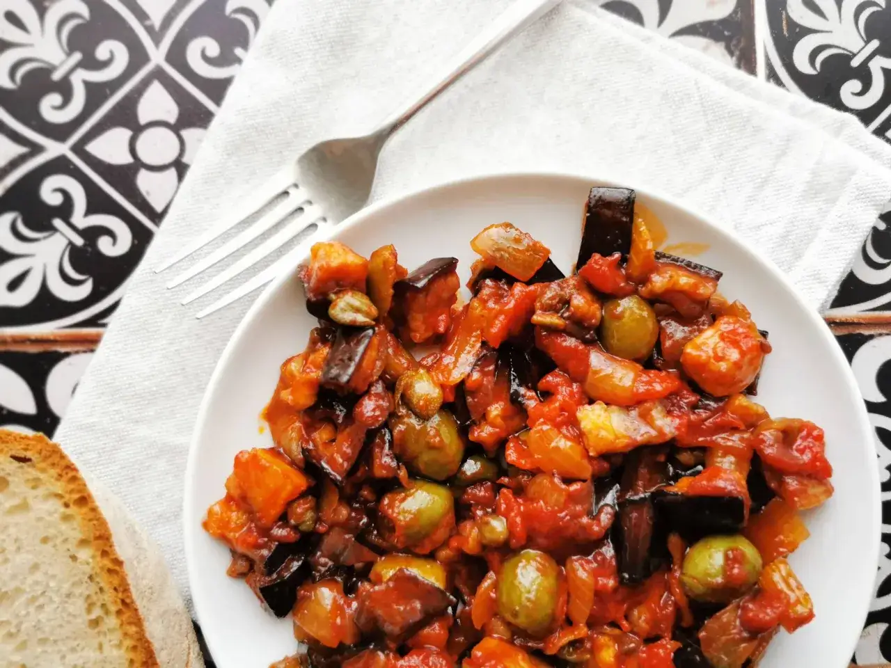 Caponata que es: un delicioso guiso siciliano de berenjenas, aceitunas y pimientos, servido con pan.