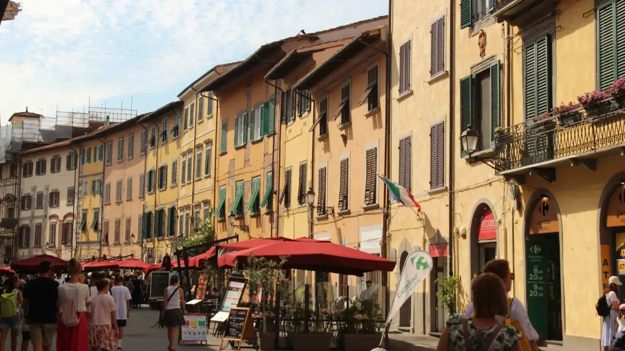 Une rue anim&eacute;e &agrave; Pise, avec des b&acirc;timents color&eacute;s, des terrasses de caf&eacute; et des passants. Id&eacute;al pour visiter Pise et fl&acirc;ner.