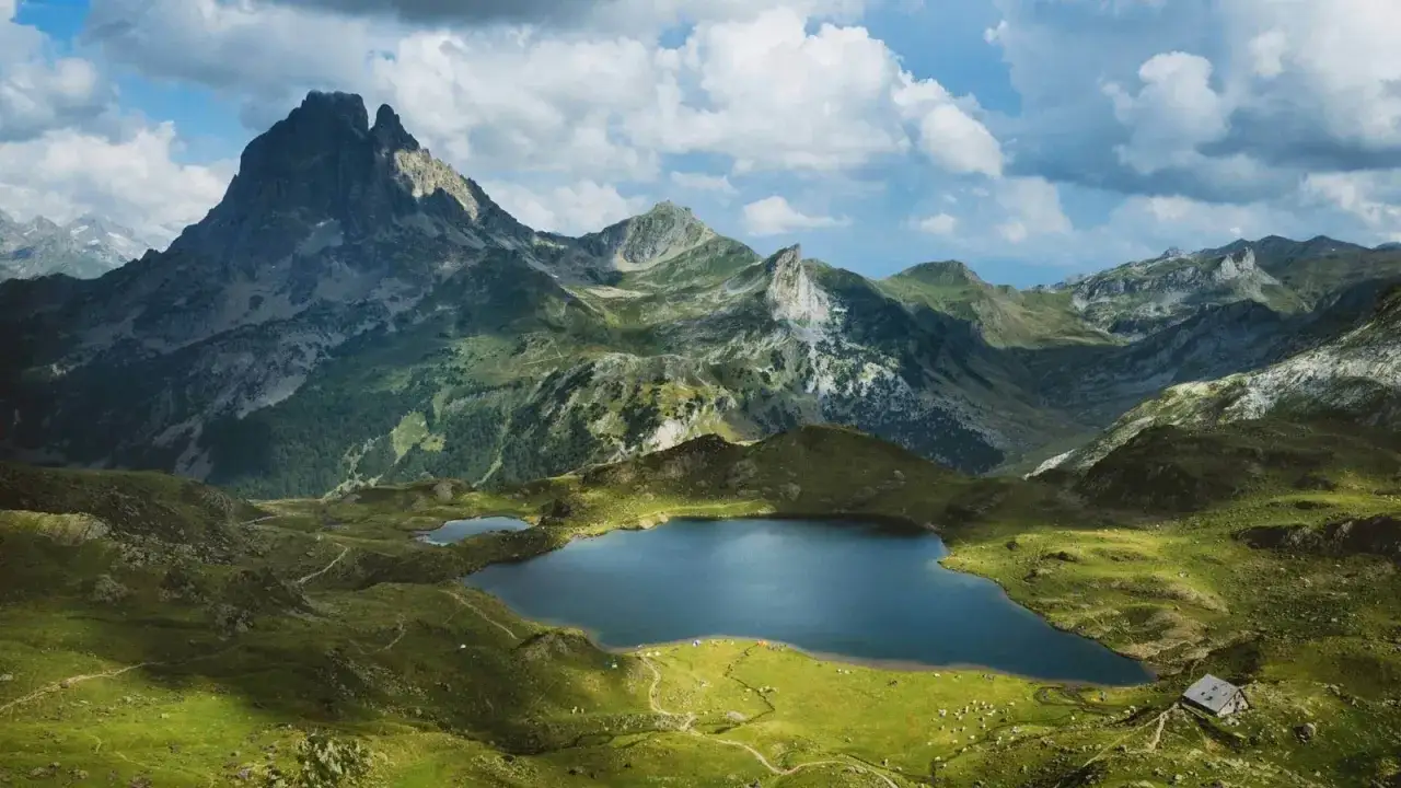 Paisaje alpino en los Pirineos Francia: un lago azul rodeado de verdes colinas y montañas imponentes bajo un cielo nublado.