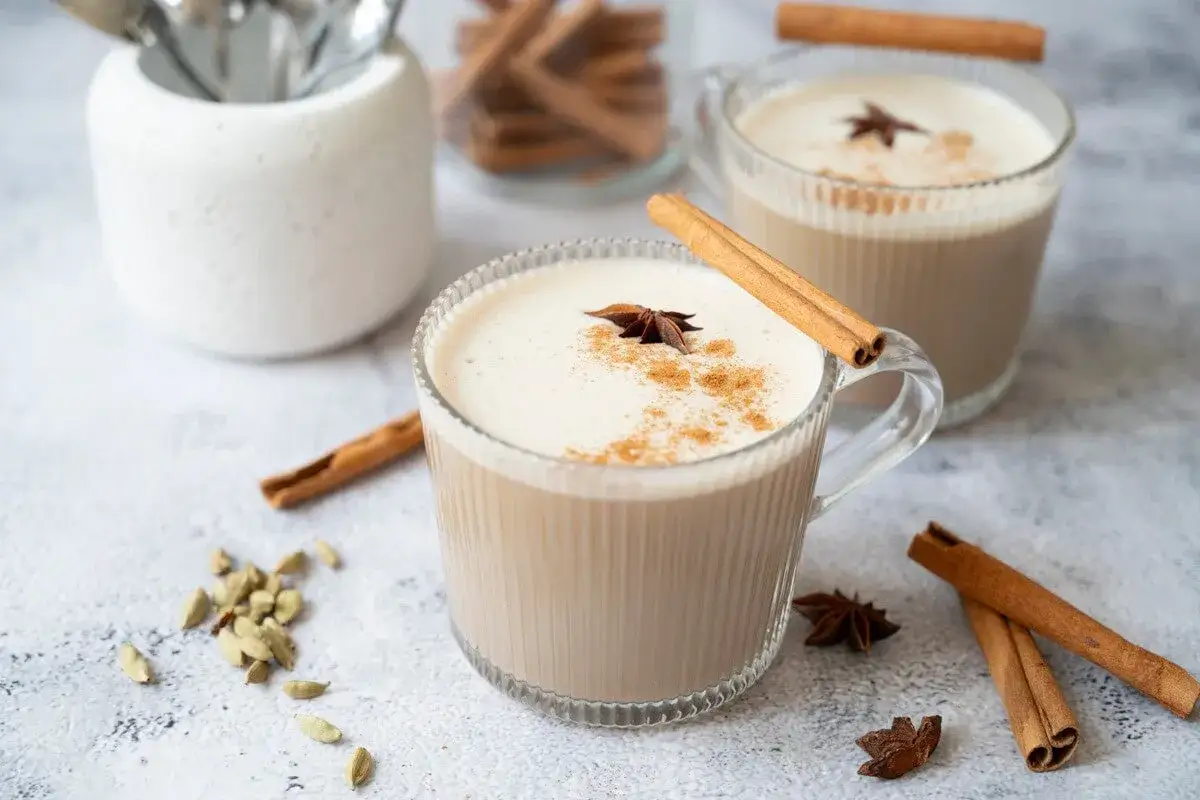 Två muggar krämig chai latte med kanelstänger och stjärnanis. Perfekt för ett mysigt chai latte recept.