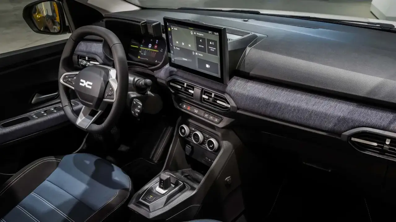 Wnętrze Dacia Sandero z ekranem dotykowym, cyfrowymi zegarami i niebiesko-czarnymi siedzeniami.