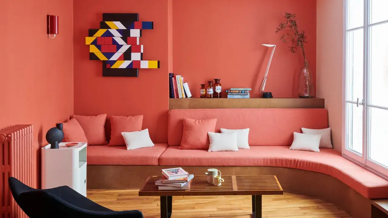 Sal&oacute;n con sof&aacute; curvo naranja, mesa de listones de madera y suelos de madera que evocan los a&ntilde;os 70. Arte abstracto en la pared.