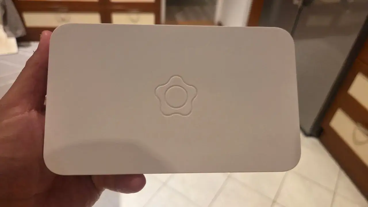 En hand h&aring;ller en vit Verisure huvudenhet med wifi. En stiliserad blomma &auml;r pr&auml;glad p&aring; ovansidan.
