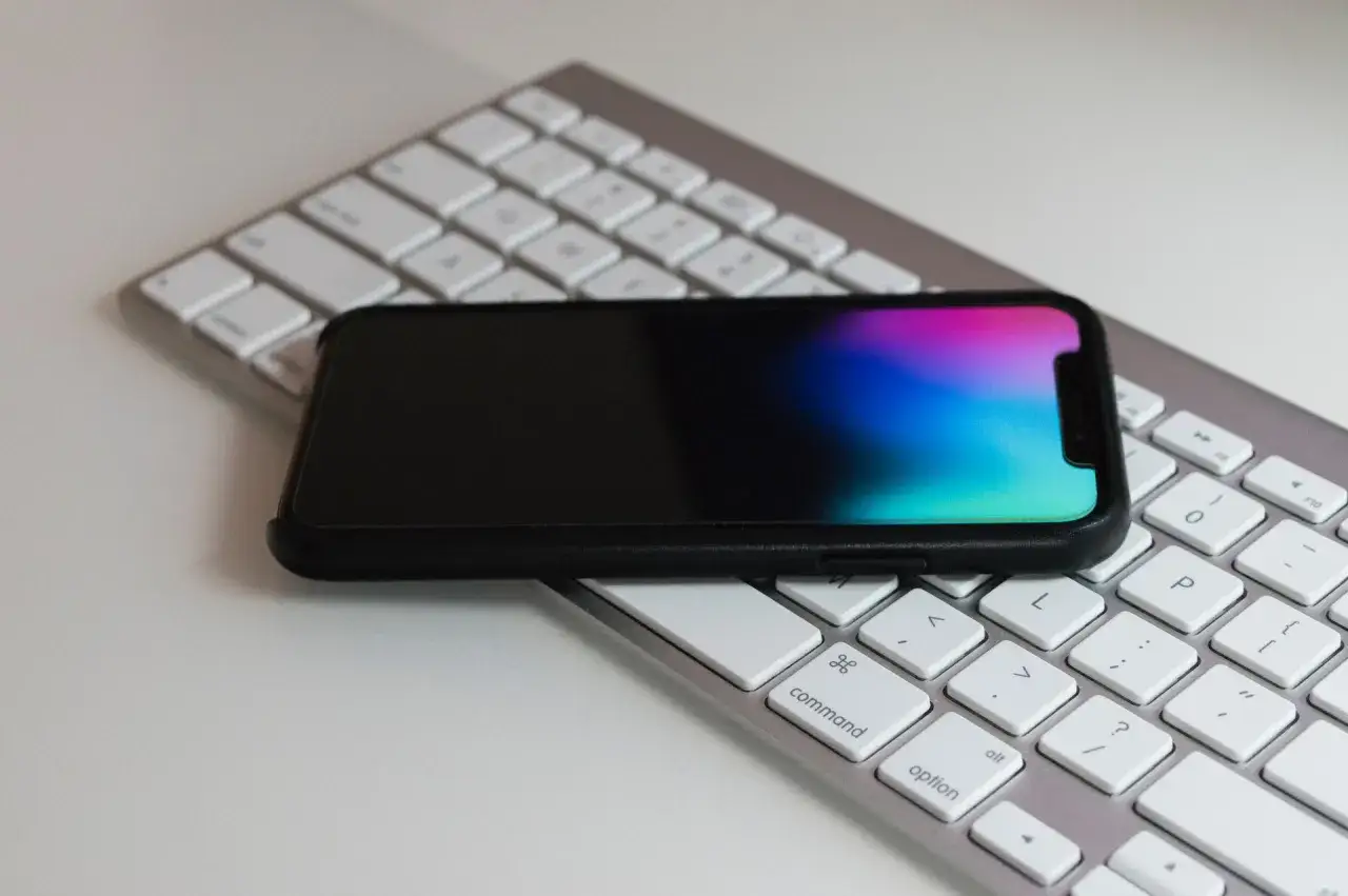 Czarny telefon leży na białej klawiaturze. Kolorowy ekran telefonu może sugerować pogorszenie jakości zdjęć w telefonie, gdy kolory stają się wyblakłe.