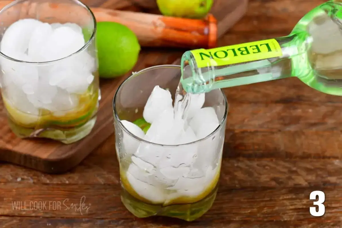 Eisw&uuml;rfel und Limettenspalten in einem Glas, w&auml;hrend Cacha&ccedil;a f&uuml;r einen Caipirinha-Lachs-Cocktail hineingegossen wird.