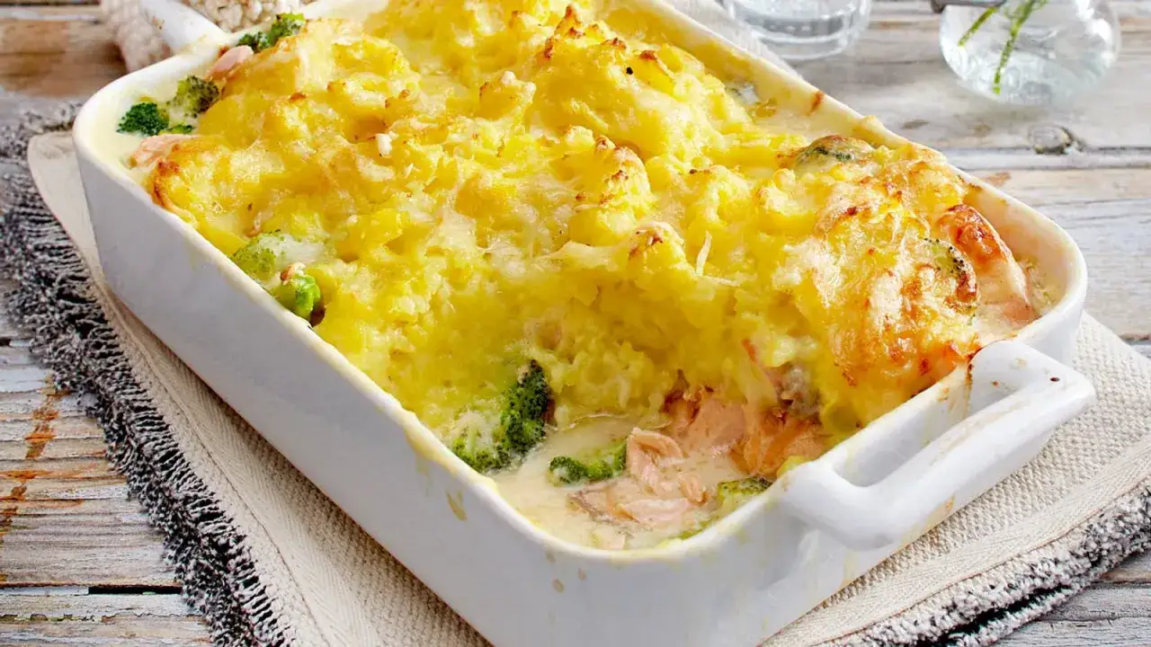 Ein k&ouml;stlicher Lachs Auflauf mit Brokkoli und einer cremigen K&auml;sekruste, serviert in einer wei&szlig;en Auflaufform auf einem rustikalen Holztisch.
