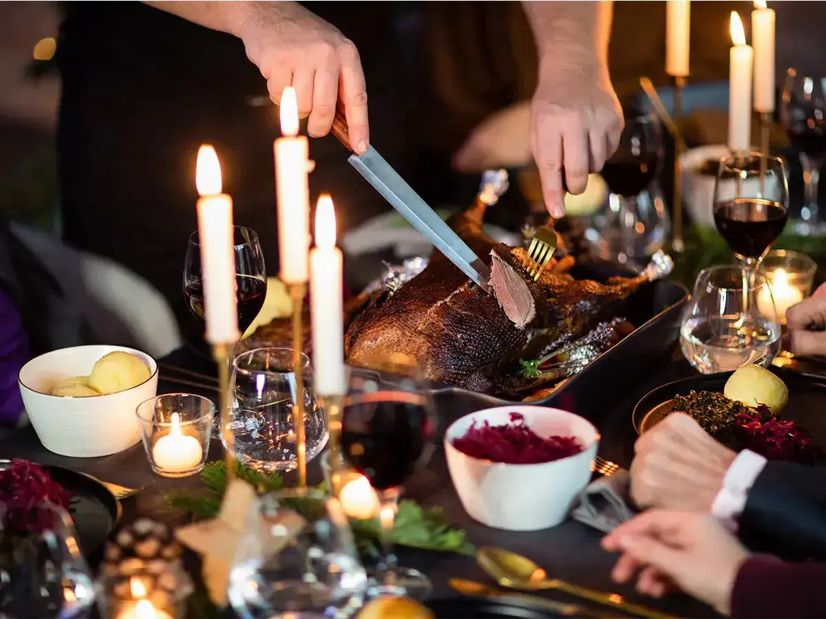 Festliches Abendessen: Ein Braten wird angeschnitten, dazu Rotwein zur Gans und Kerzenlicht.