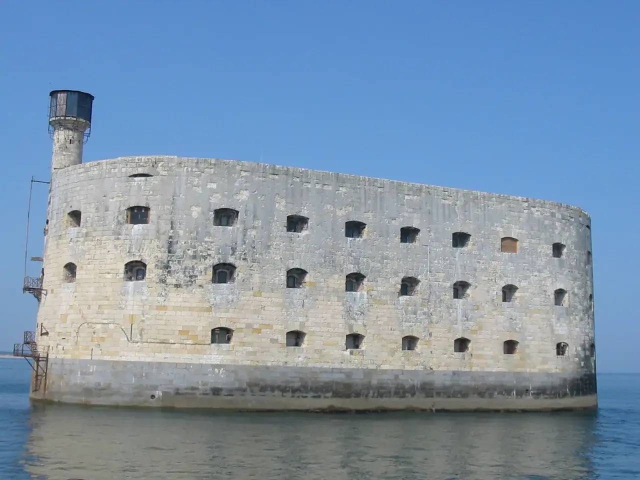 Fort Boyard, potężna twierdza na morzu, z licznymi oknami i wieżą, otoczona spokojną wodą.
