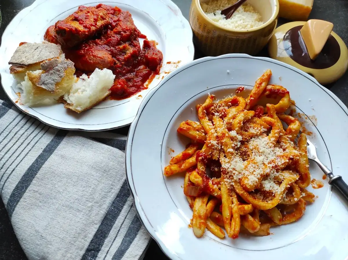 Pyszne maccheroni al ferretto w sosie pomidorowym, obok talerz mięsa w sosie i chlebka.
