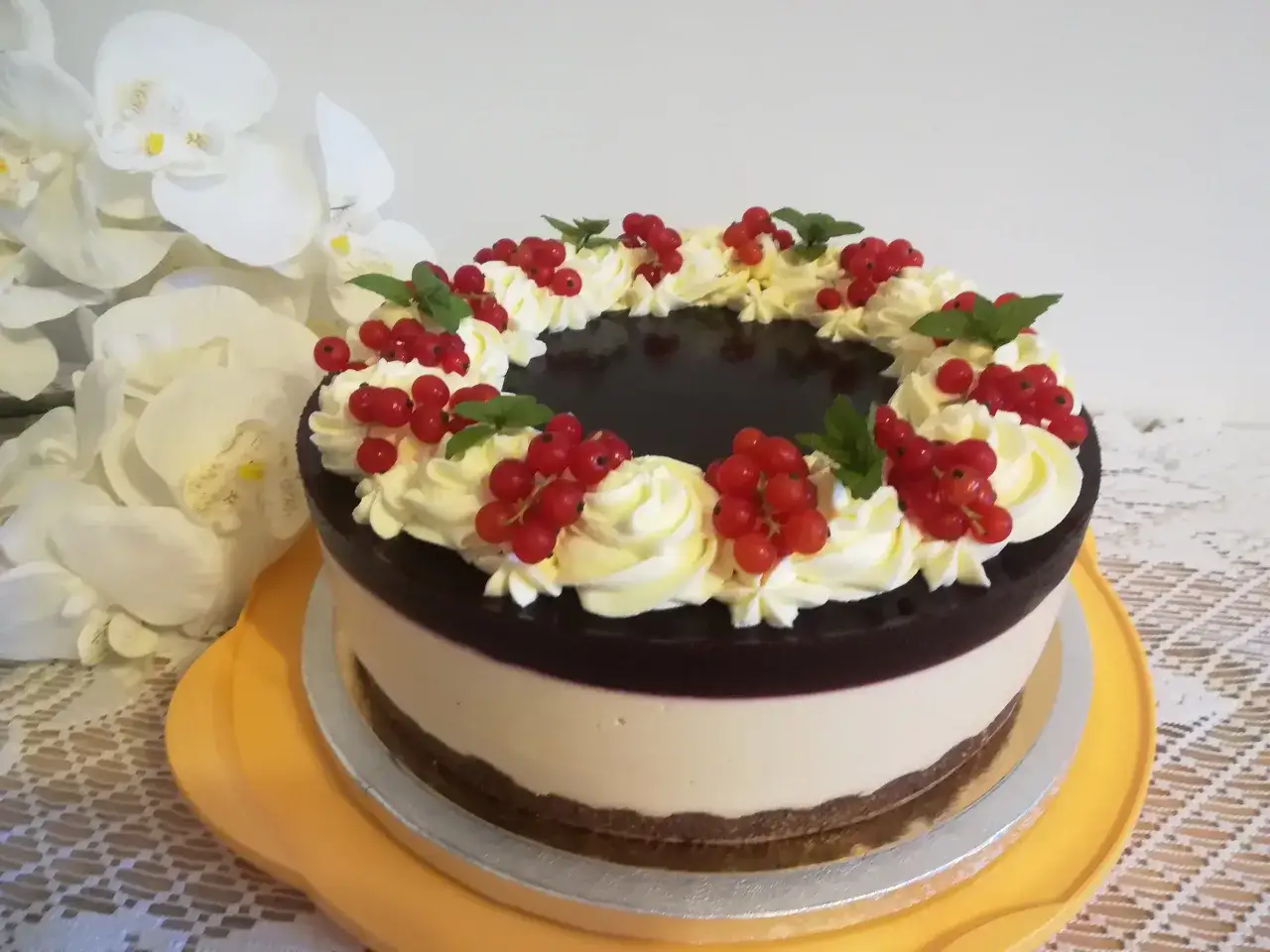 Elegancki tort z warstwą musu, ciemną galaretką i dekoracją z bitej śmietany, świeżych czerwonych porzeczek i listków mięty. Na wierzchu błyszcząca frużelina z czarnej porzeczki.