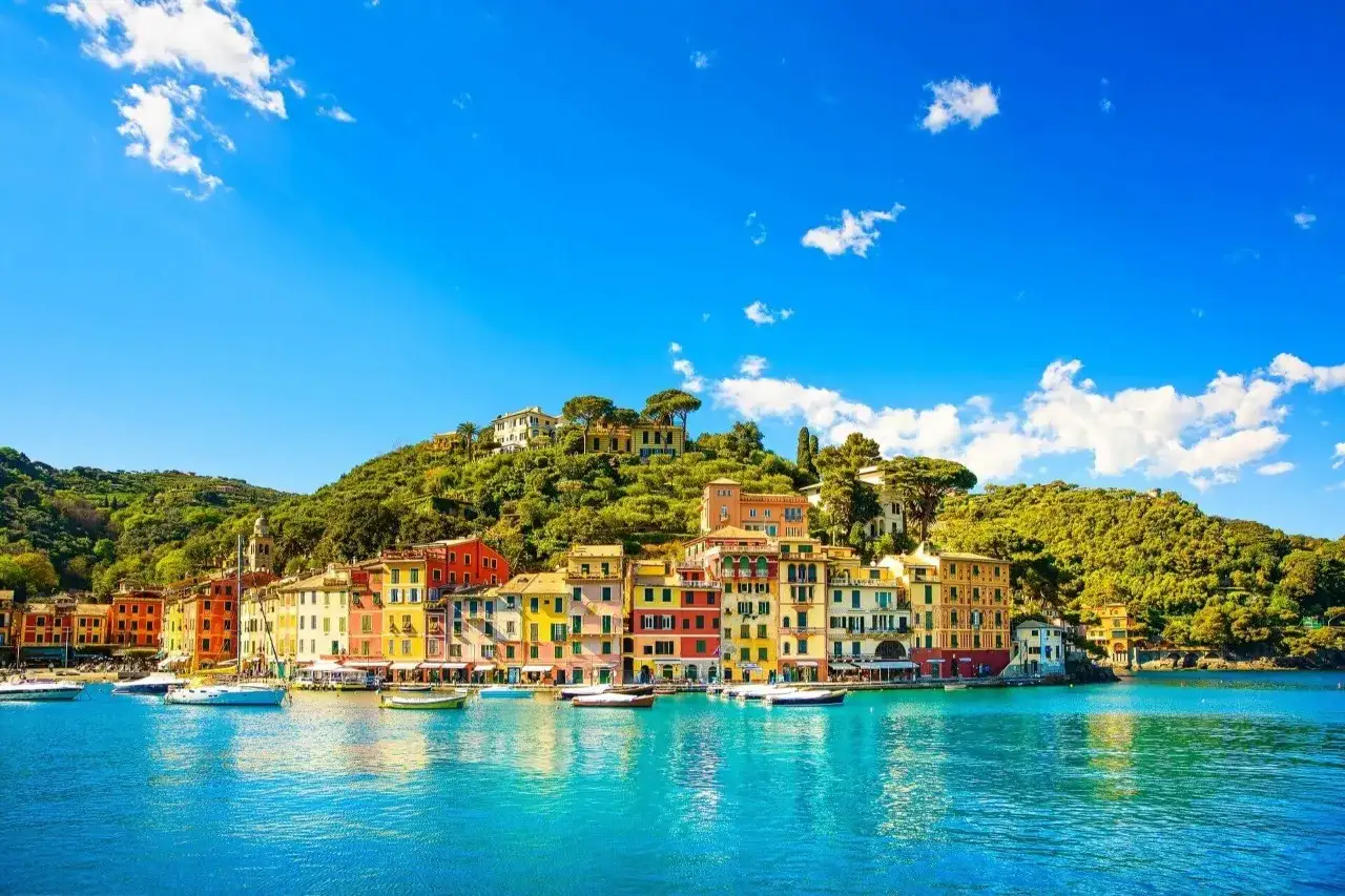 Bunte H&auml;user s&auml;umen die K&uuml;ste von Portofino, Italien, mit Booten im t&uuml;rkisfarbenen Wasser vor einer &uuml;ppig gr&uuml;nen H&uuml;gellandschaft.
