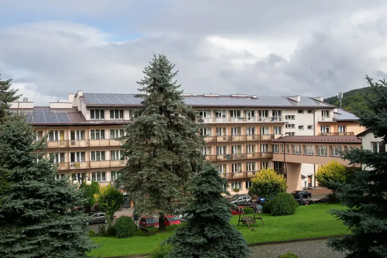 Sanatorium Górnik w Iwoniczu Zdroju, z panelami słonecznymi na dachu, otoczone zielenią i drzewami.