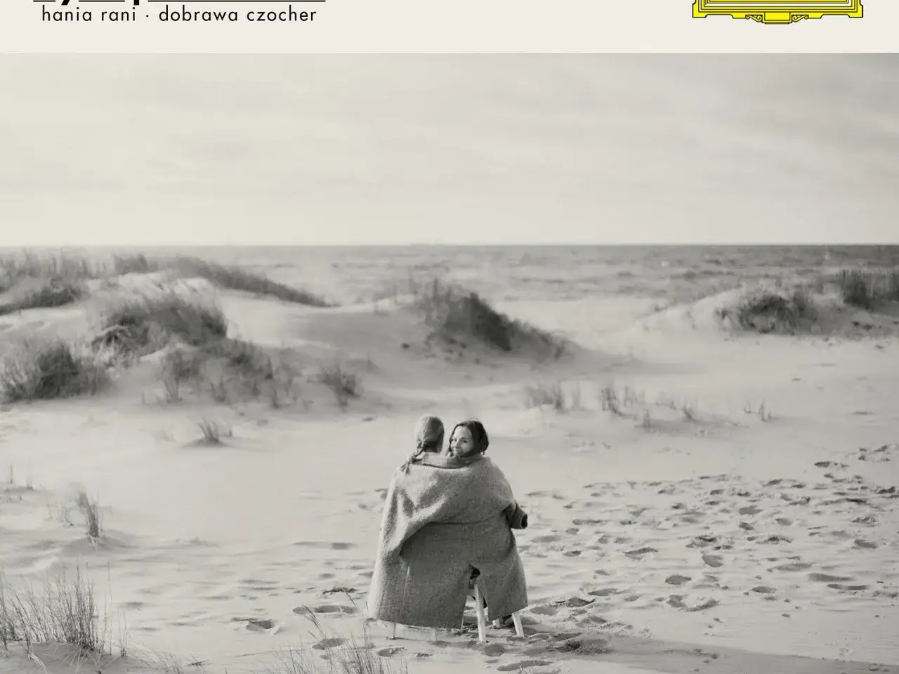 Dwie kobiety otulone kocem na plaży, słuchają muzyki Hani Rani. Ich 