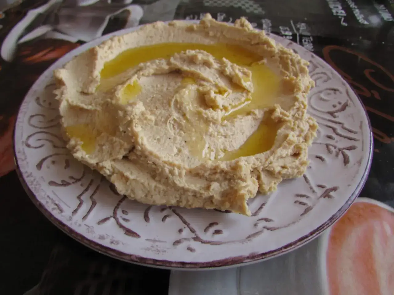 Puszysty, kremowy hummus polany oliwą na ozdobnym talerzu. To pyszne danie, które warto znać!