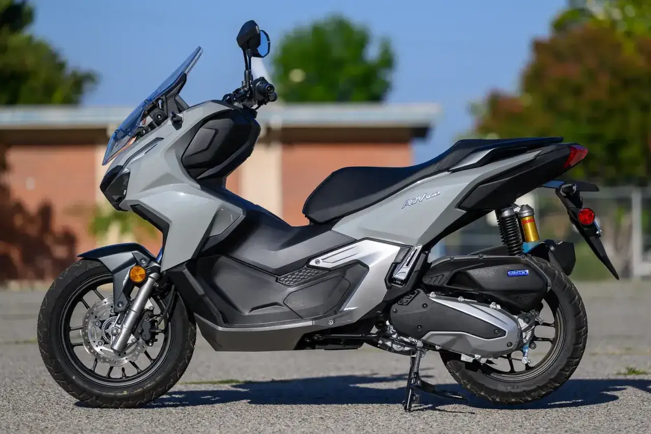Scooter gris Honda ADV 160 aparcada en exteriores, con detalles en negro y amortiguadores dorados.