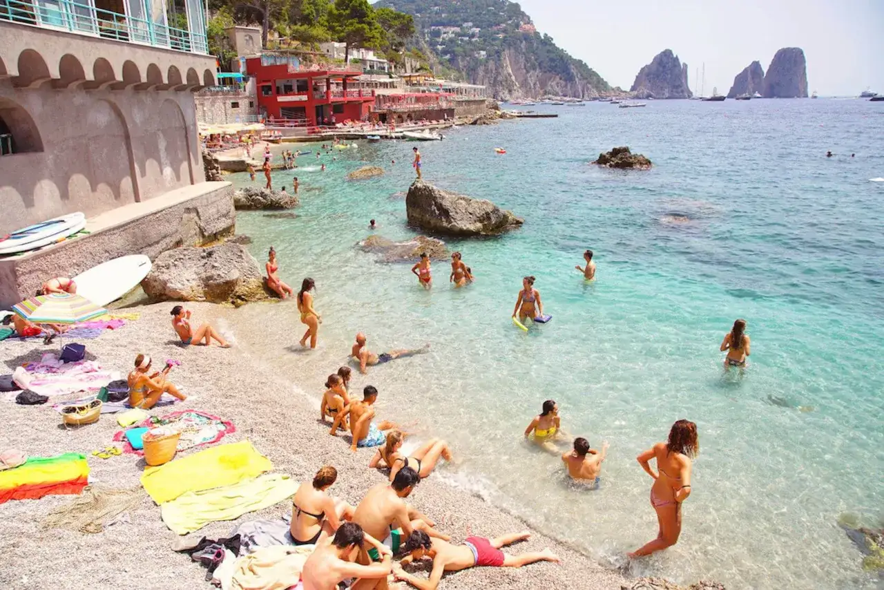 Gente in costume da bagno si rilassa e nuota nella spiaggia di Marina Piccola, con acque cristalline e rocce.
