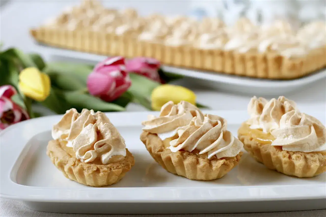 Pyszne babeczki z kremem bezowym, idealne, gdy zastanawiasz się, co zrobić z żółtek. W tle prostokątna tarta i kolorowe tulipany.