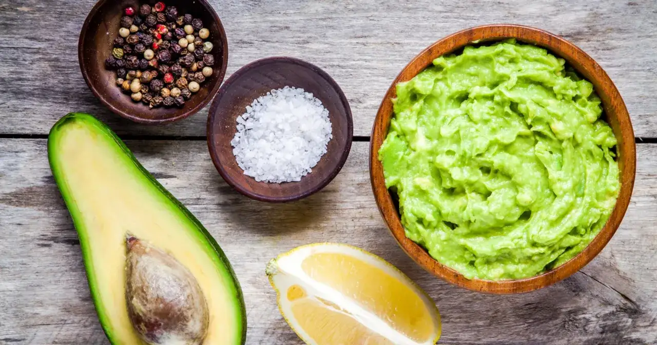 Awokado, tropikalny owoc o dużej zawartości tłuszczu, w misce jako guacamole, obok cytryny, soli i pieprzu.
