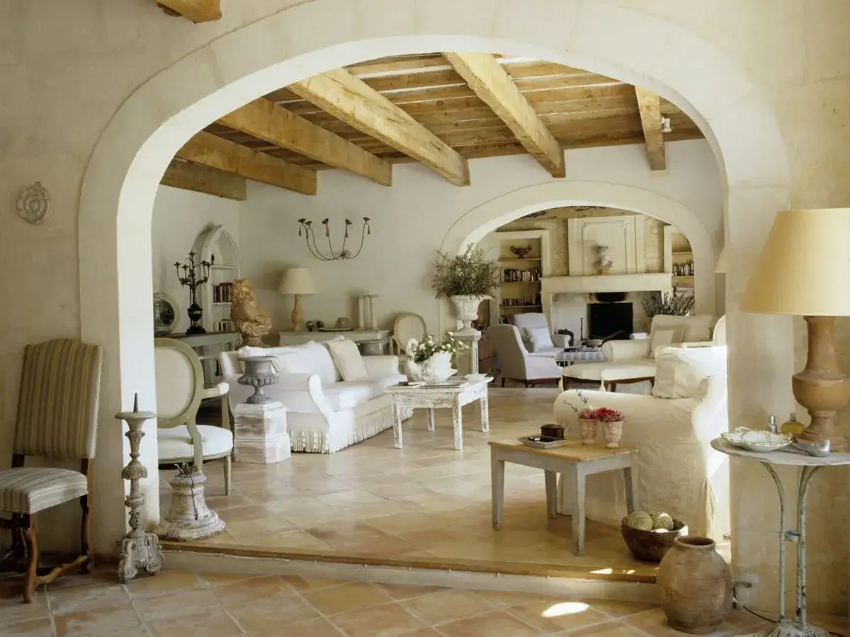 Salotto in **stile provenzale francese** con divani bianchi, travi a vista e pavimenti in cotto.