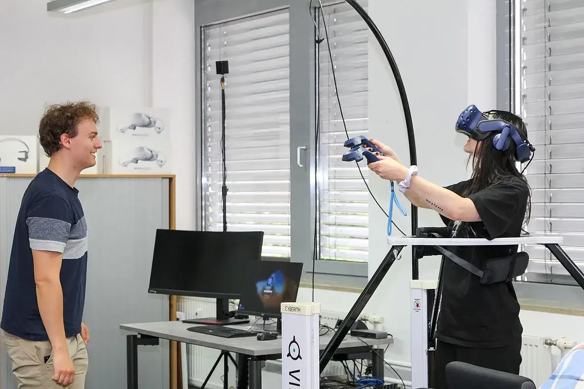 Ein Mann beobachtet eine Frau, die eine VR-Brille tr&auml;gt und Controller h&auml;lt. Hier wird gelebt, was ist Medieninformatik: Interaktion mit virtuellen Welten.