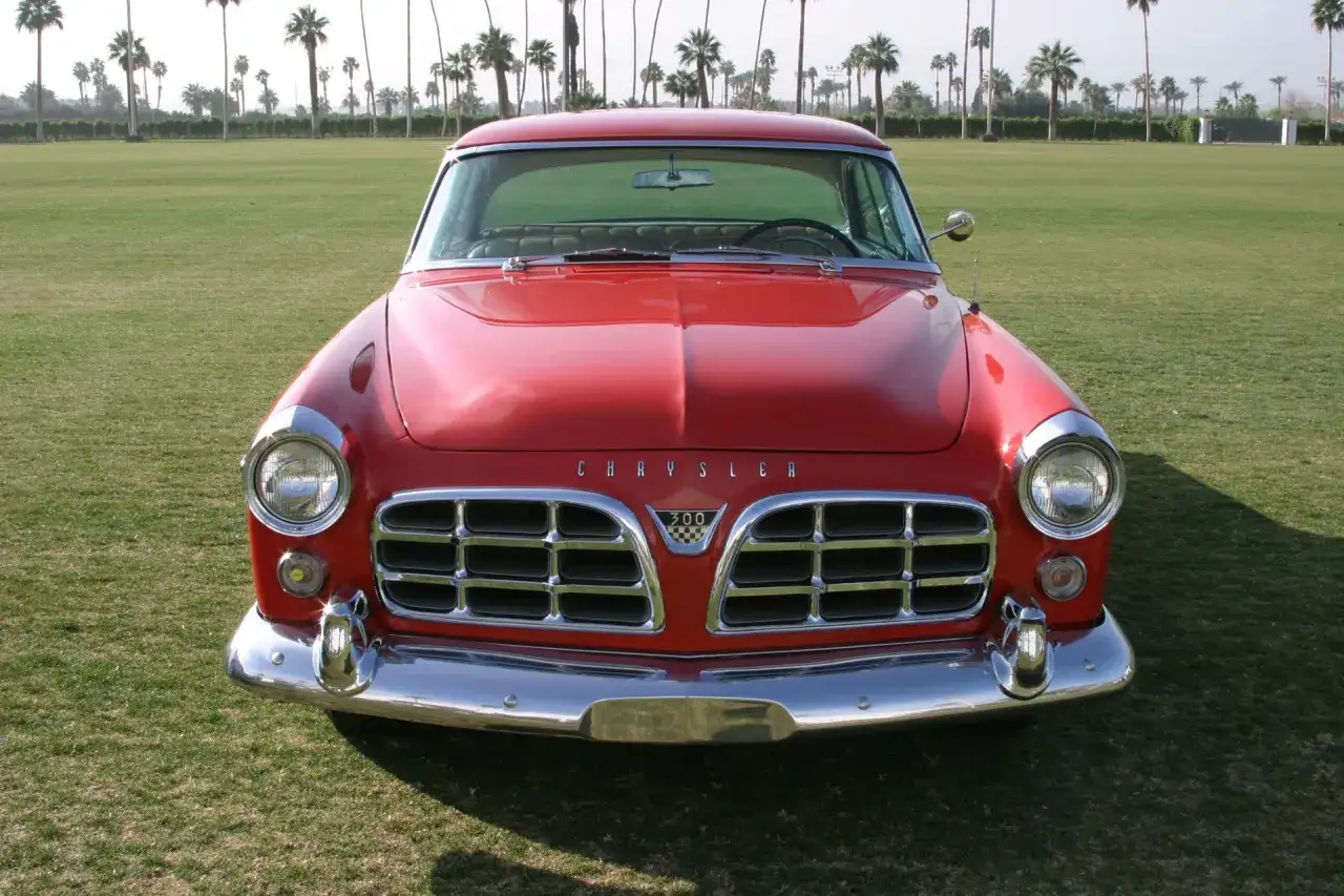 Röd Chrysler 300 från 1950-talet parkerad på en gräsmatta med palmer i bakgrunden.