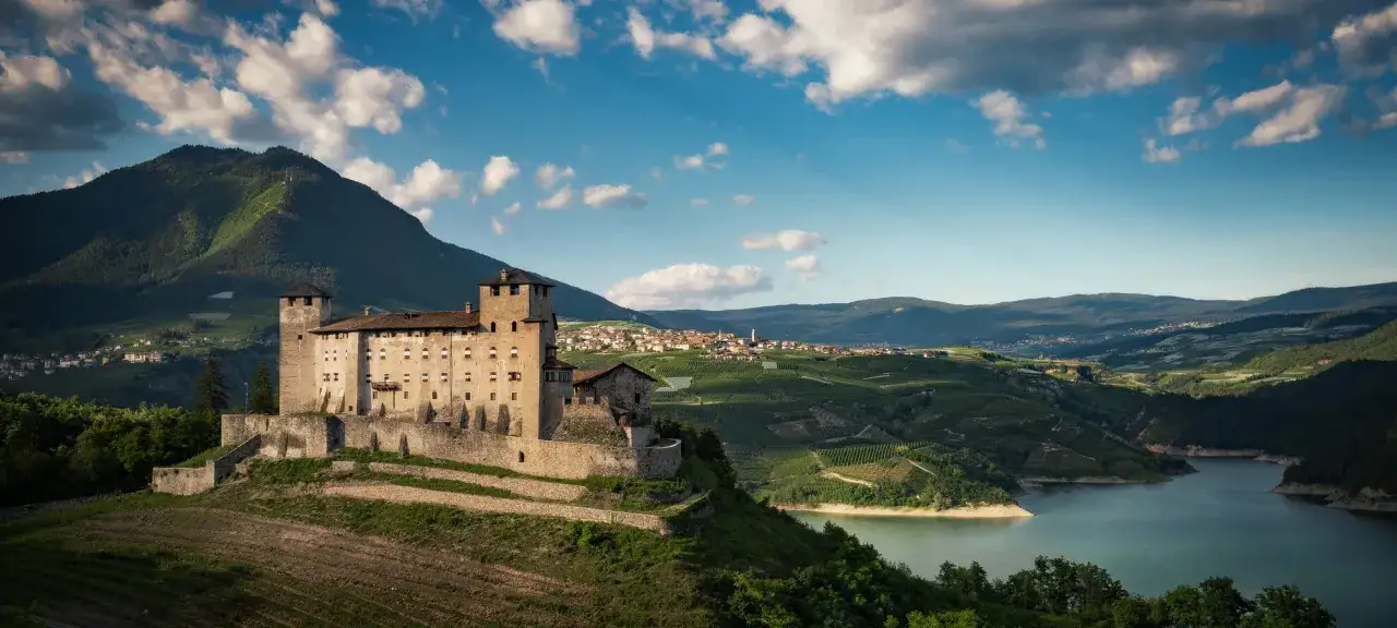 Castello medievale domina un paesaggio di vigneti e laghi, con borghi pittoreschi nei **paesi Val di Non**.
