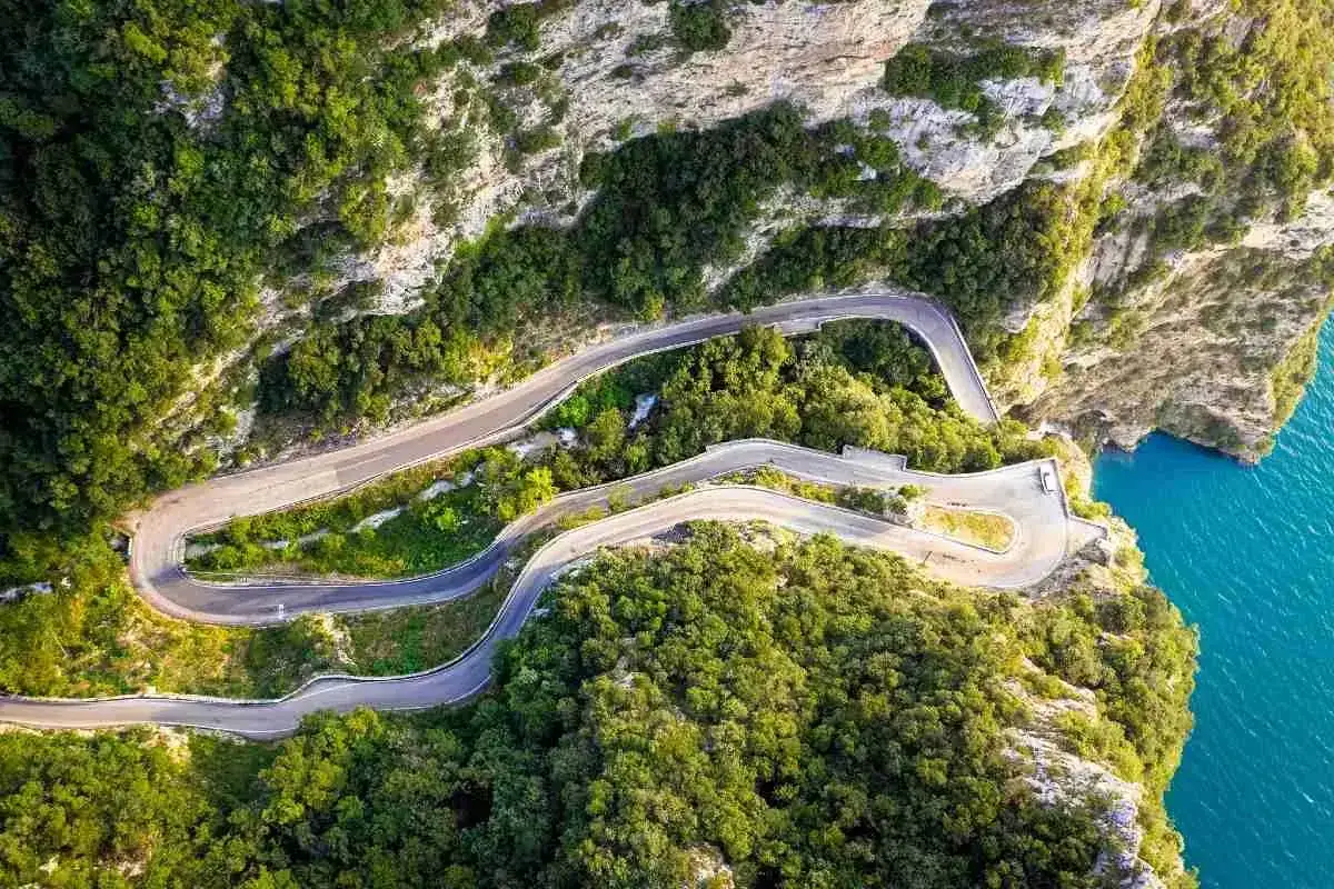 Strada della forra in moto, un nastro d'asfalto serpeggia tra rocce e vegetazione lussureggiante, con il mare azzurro a picco.