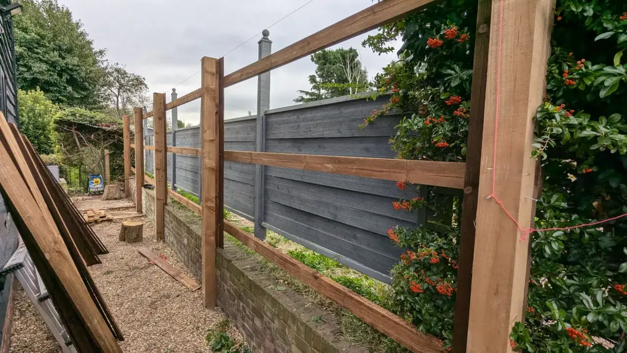 A new metal fence installation is underway, with wooden posts and horizontal beams forming the structure.