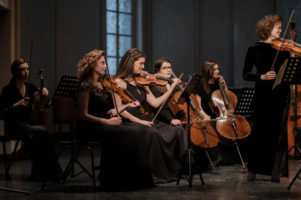 Kobiety w czarnych sukniach grają na skrzypcach i wiolonczelach. Ich muzyka to piękna oda do sztuki.