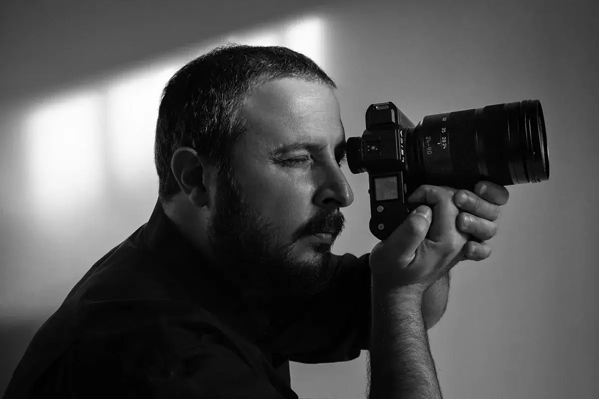 Uomo con barba guarda attraverso la fotocamera Leica, un'ispirazione per una foto aesthetic da fare.