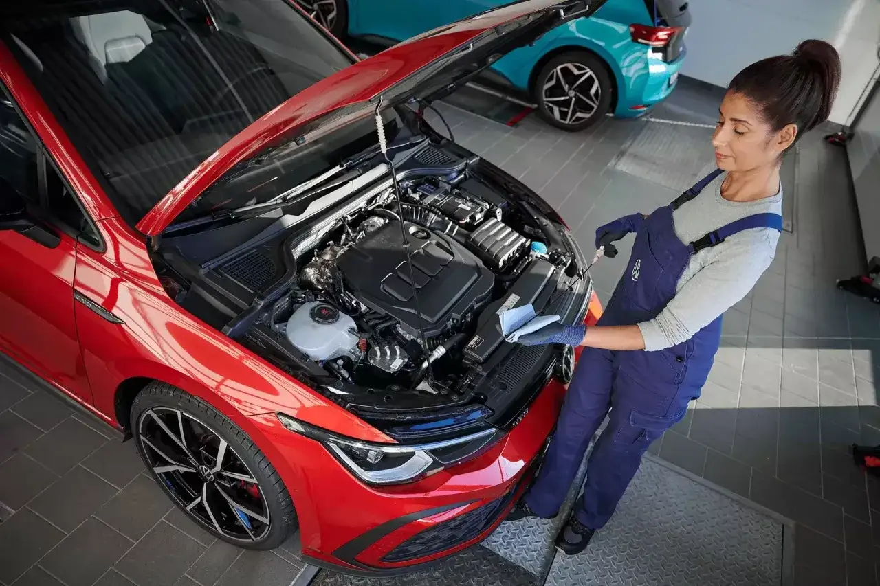 Mechanik sprawdza poziom oleju w czerwonym VW. Dowiedz się, ile kosztuje wymiana oleju w ASO VW.