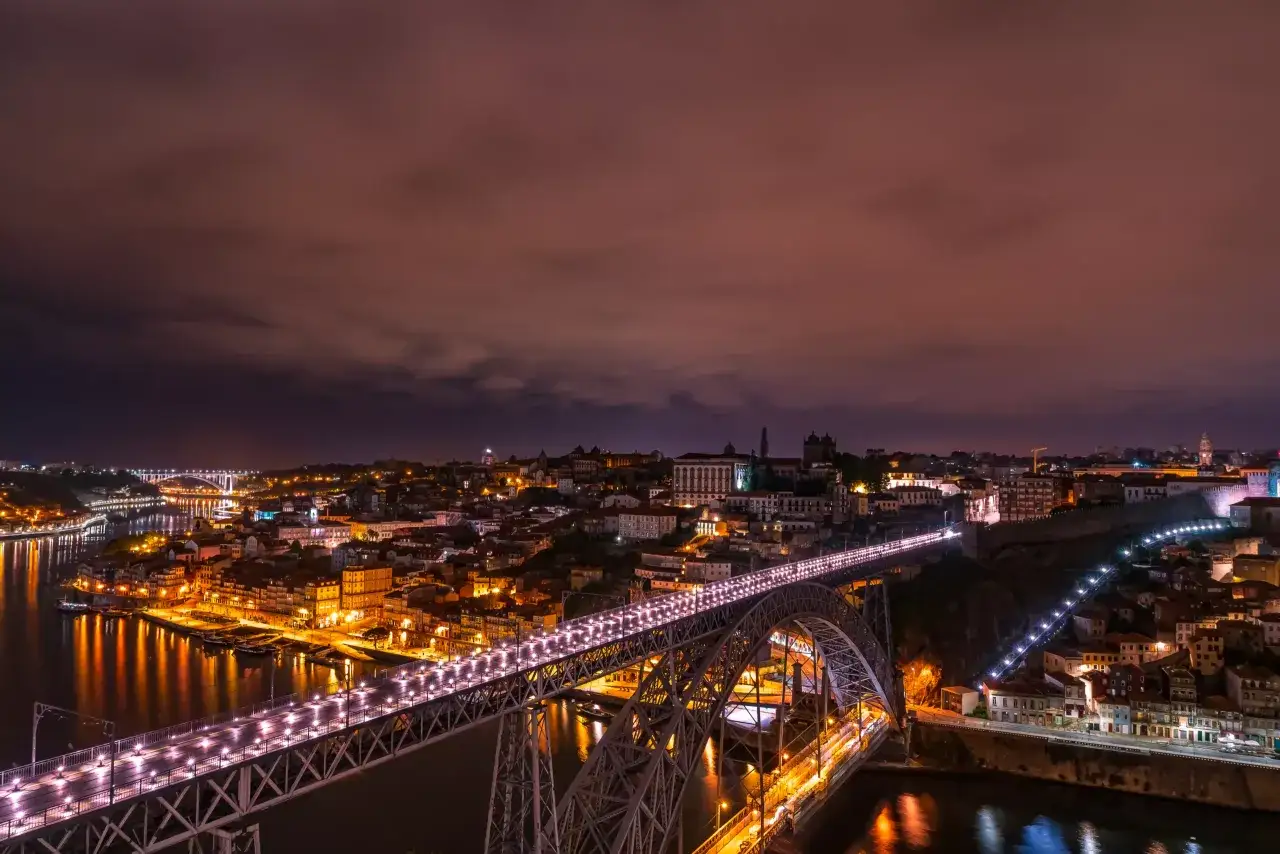 Nocny widok na Porto, z mostem Dom Luís I oświetlonym tysiącami świateł. Miasto lśni nad rzeką Duero, tworząc magiczną atmosferę.