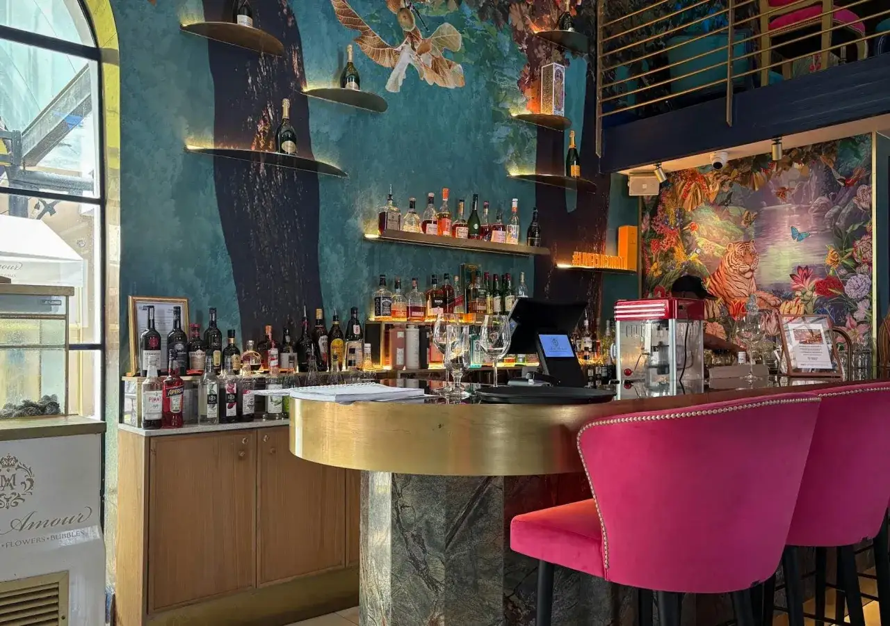 Un locale con un'atmosfera da basic club Napoli, con un bancone dorato, sgabelli fucsia e un murale di tigri e natura esotica.