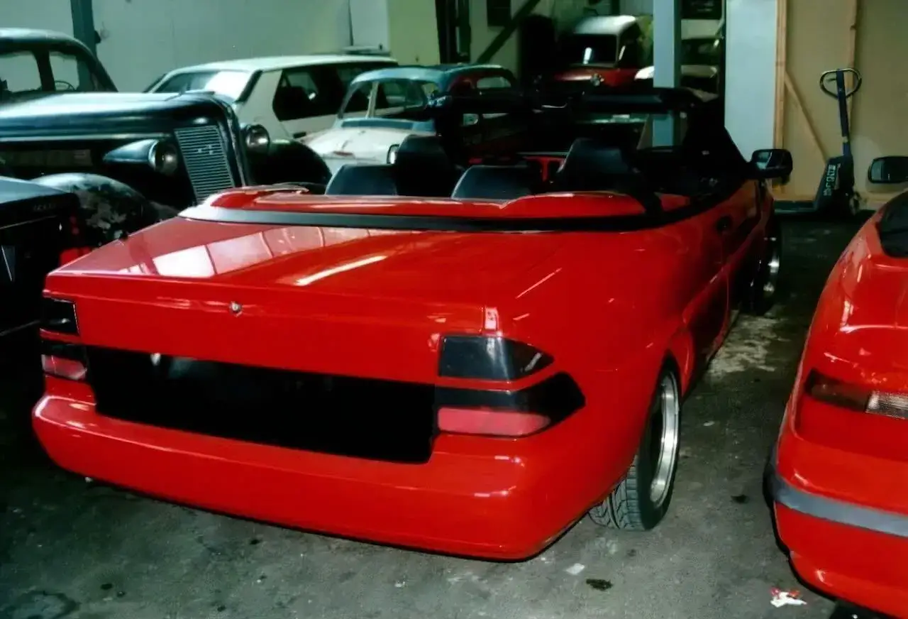 Röd Saab 9000 cabriolet i garage, med andra bilar i bakgrunden.