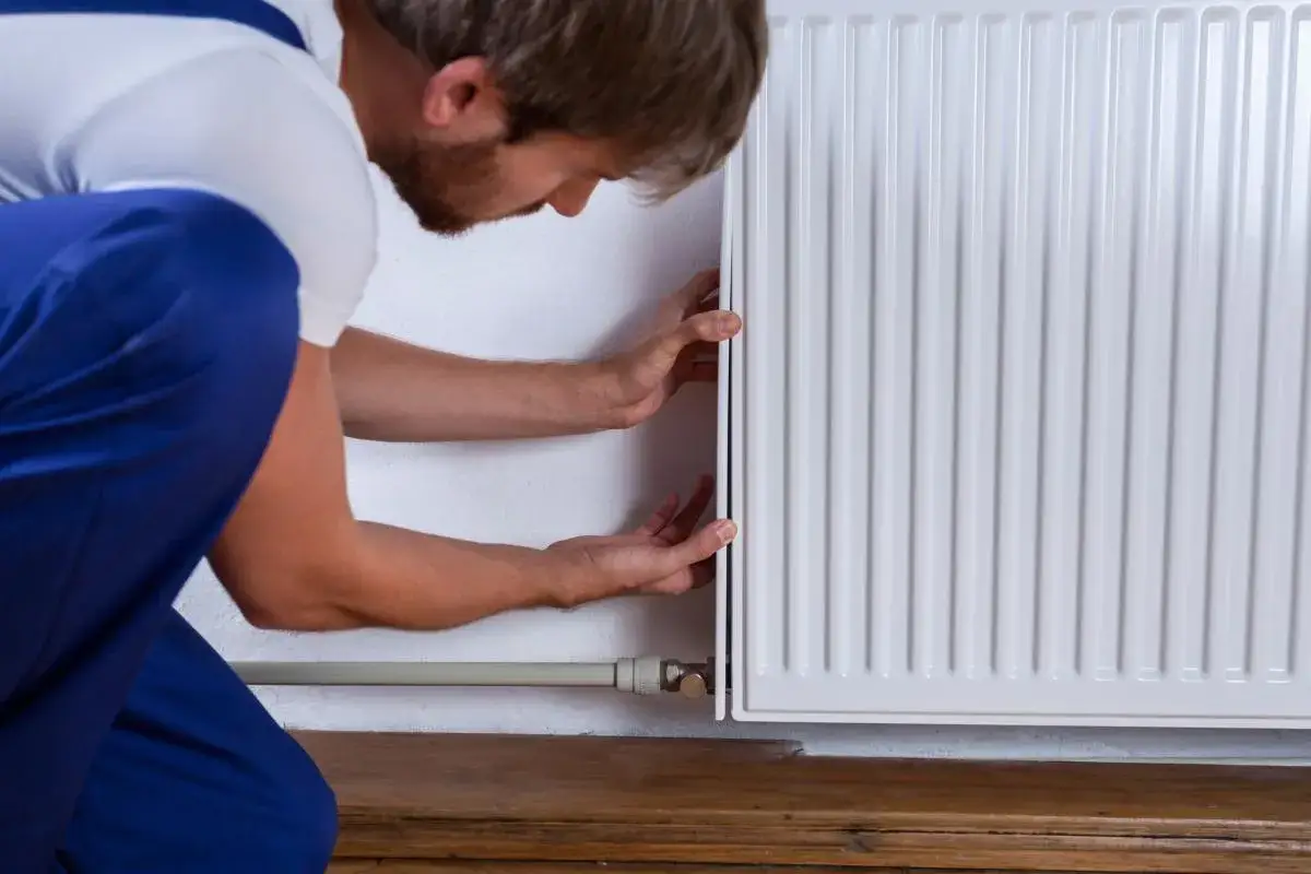 Técnico revisa un radiador blanco, asegurándose de que no calienta. Sus manos ajustan el panel.