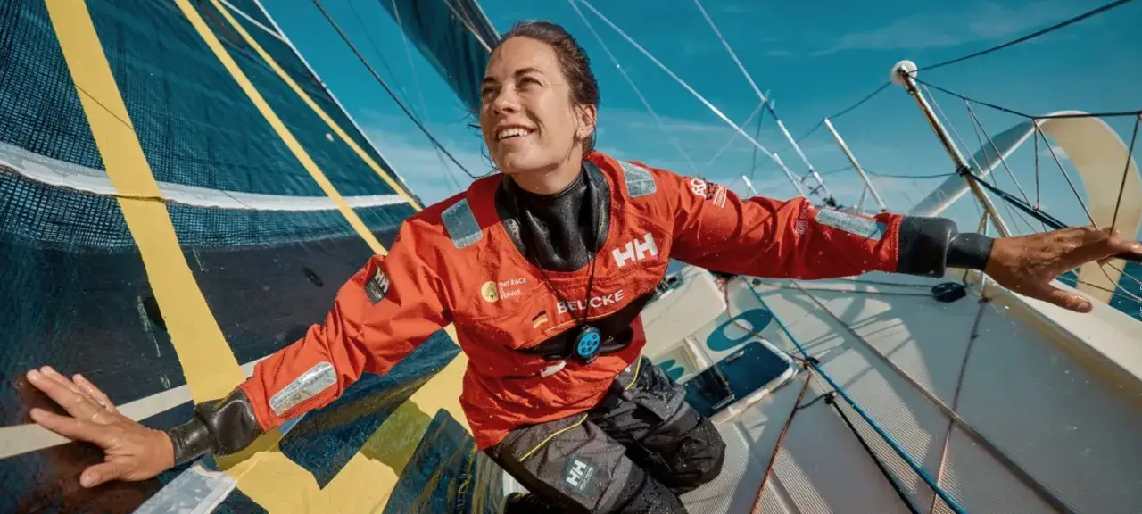 Sanni Beucke strahlt auf dem Segelboot, die H&auml;nde auf dem Gro&szlig;segel.