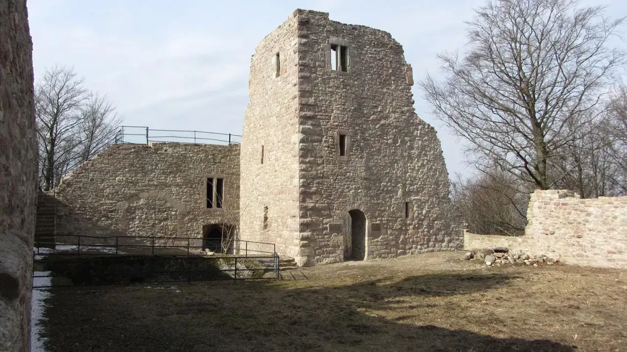 Ruinen einer Burg, die von Hütten umgeben ist, mit einem hohen Turm und Mauern aus Stein.