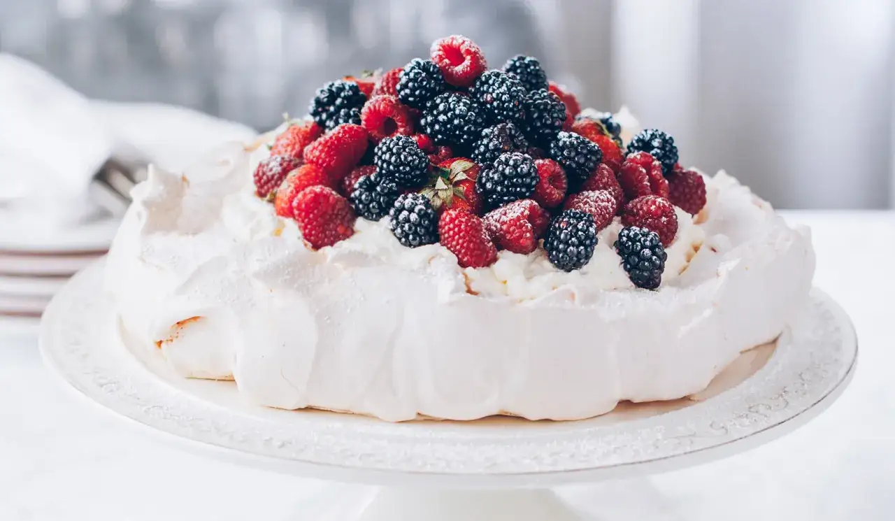 Beza pavlova która zawsze wychodzi, udekorowana bitą śmietaną i mnóstwem świeżych malin i jeżyn.