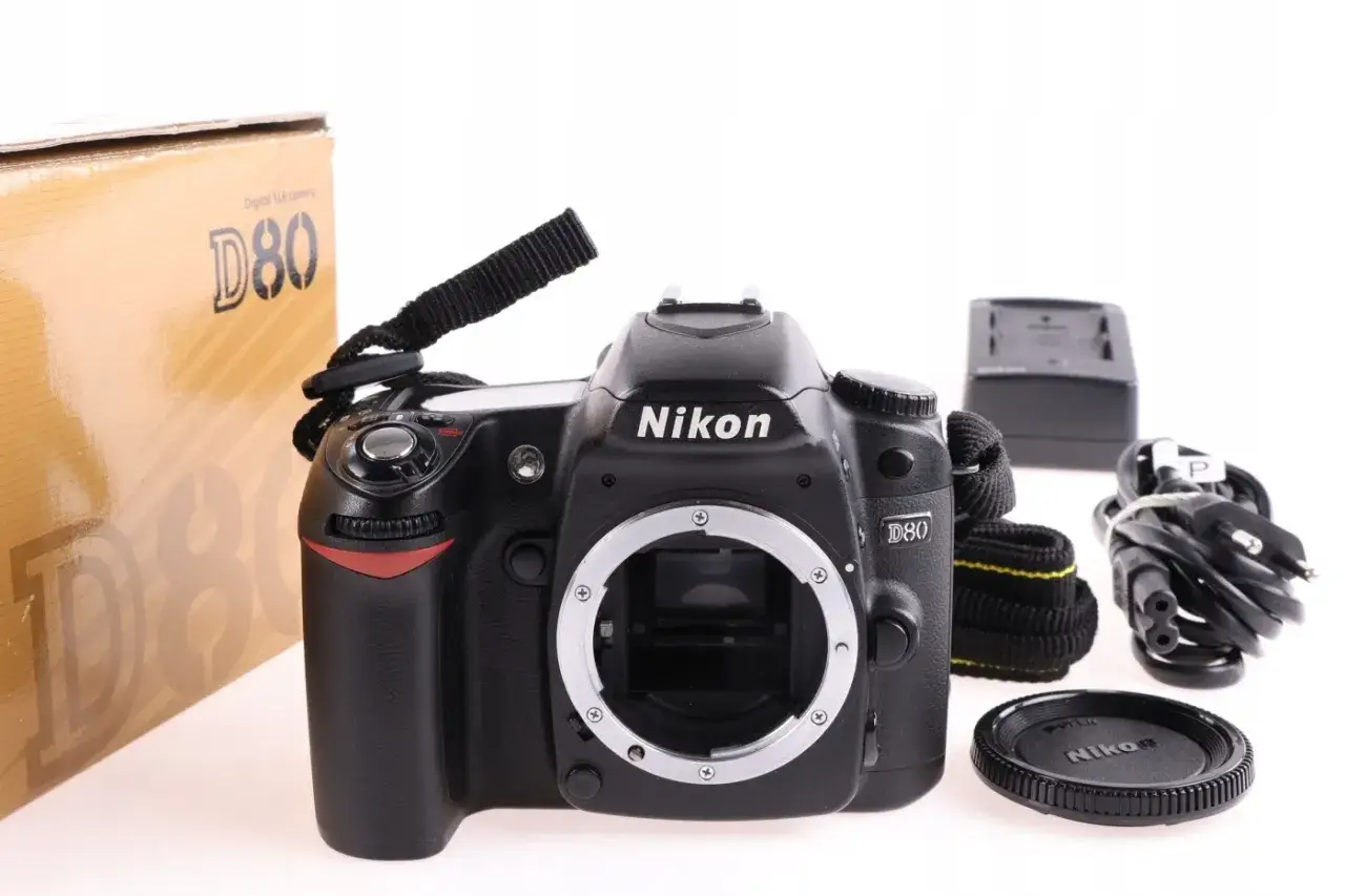 Zestaw z aparatem Nikon D80: korpus, ładowarka, kable, pasek i dekielek.