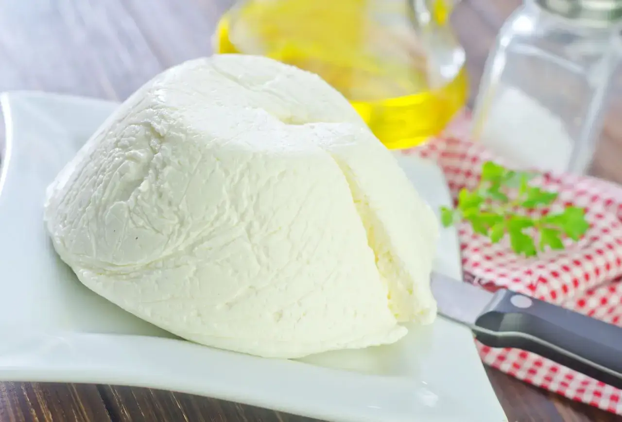 Świeża ricotta na talerzu, gotowa do podania. Jej delikatny smak zachwyci każdego. Obok oliwa, s&oacute;l i natka pietruszki.