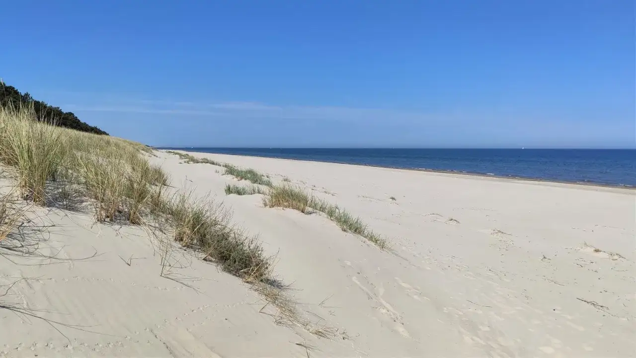Plaża Ulinia: piaszczyste wydmy porośnięte trawami, spokojne morze i błękitne niebo. Idealne miejsce na spacer.