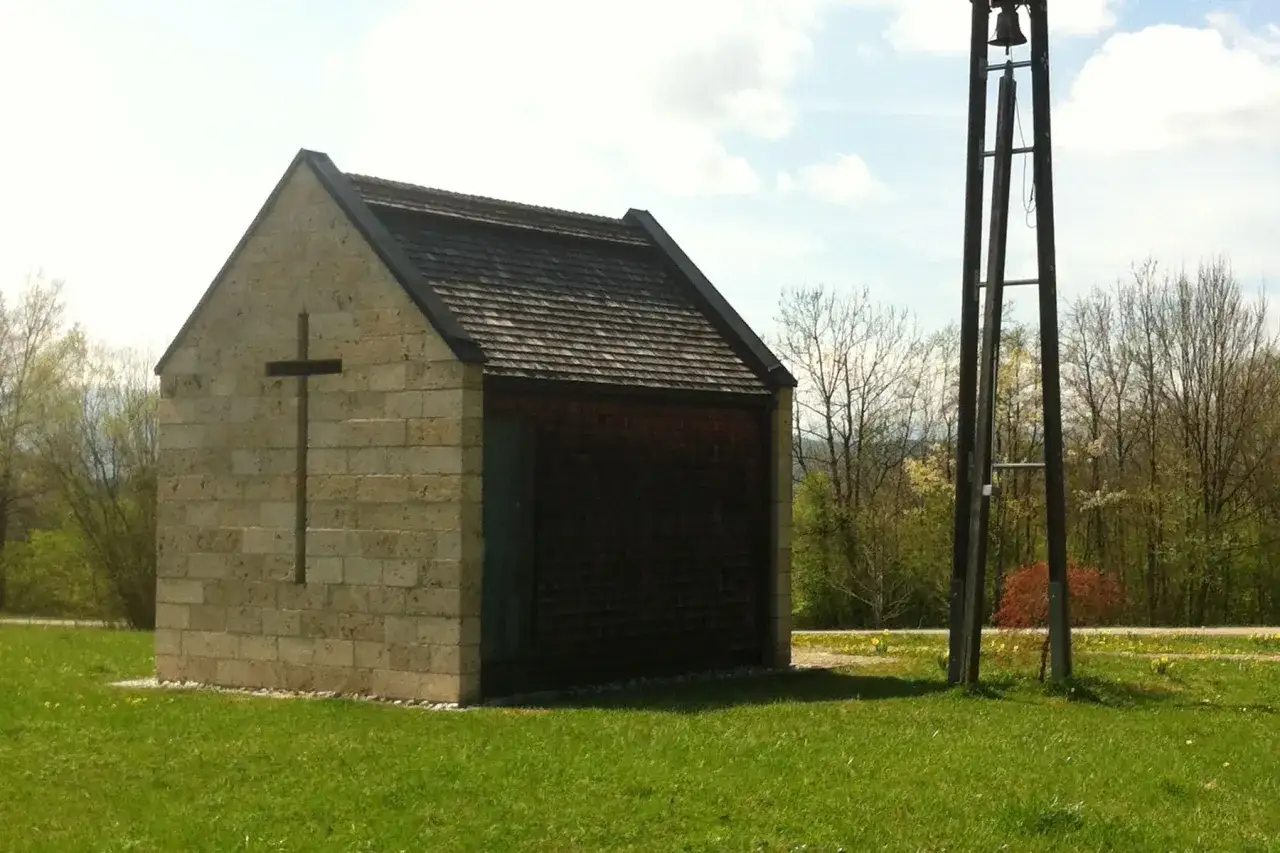 Kleine Barbara Kapelle aus Stein mit Holzdach, daneben ein Glockenturm.