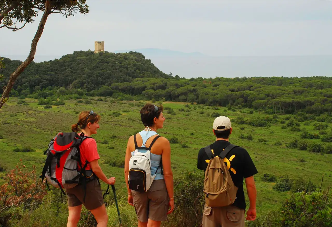 Tre escursionisti ammirano il panorama del Parco Regionale della Maremma, con una torre in lontananza.