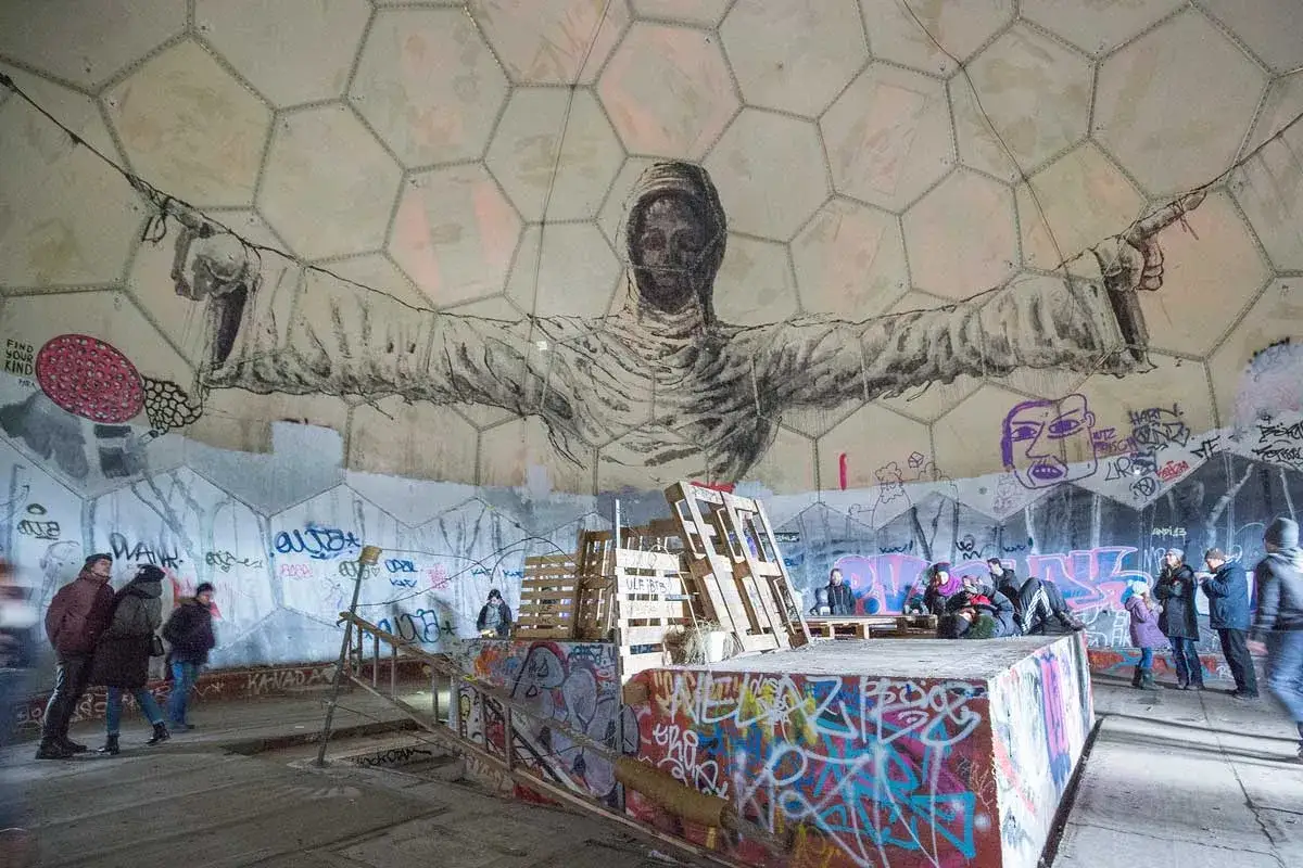 Besucher bestaunen die Kunst im Inneren des Teufelsberg Berlin. Graffiti bedeckt die W&auml;nde und eine riesige Figur dominiert die Kuppel.