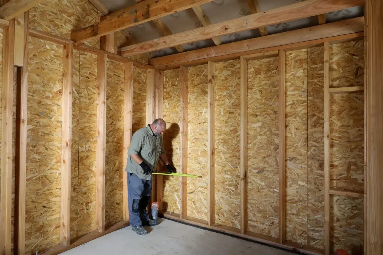 Un homme mesure un mur en panneaux OSB, soulignant la **résistance thermique bois** pour une construction efficace.