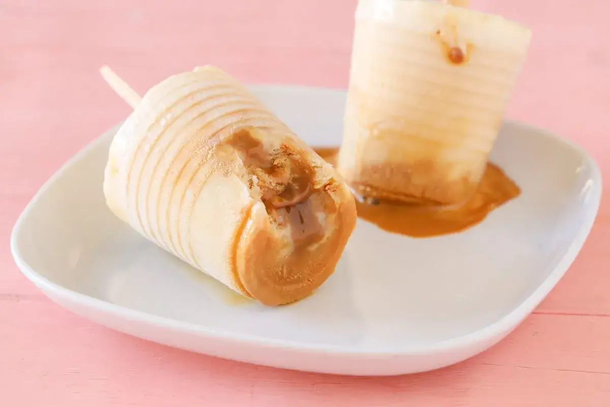 Dos helados de dulce de leche, uno mordido, sobre un plato blanco. El dulce de leche se derrama, tentador.
