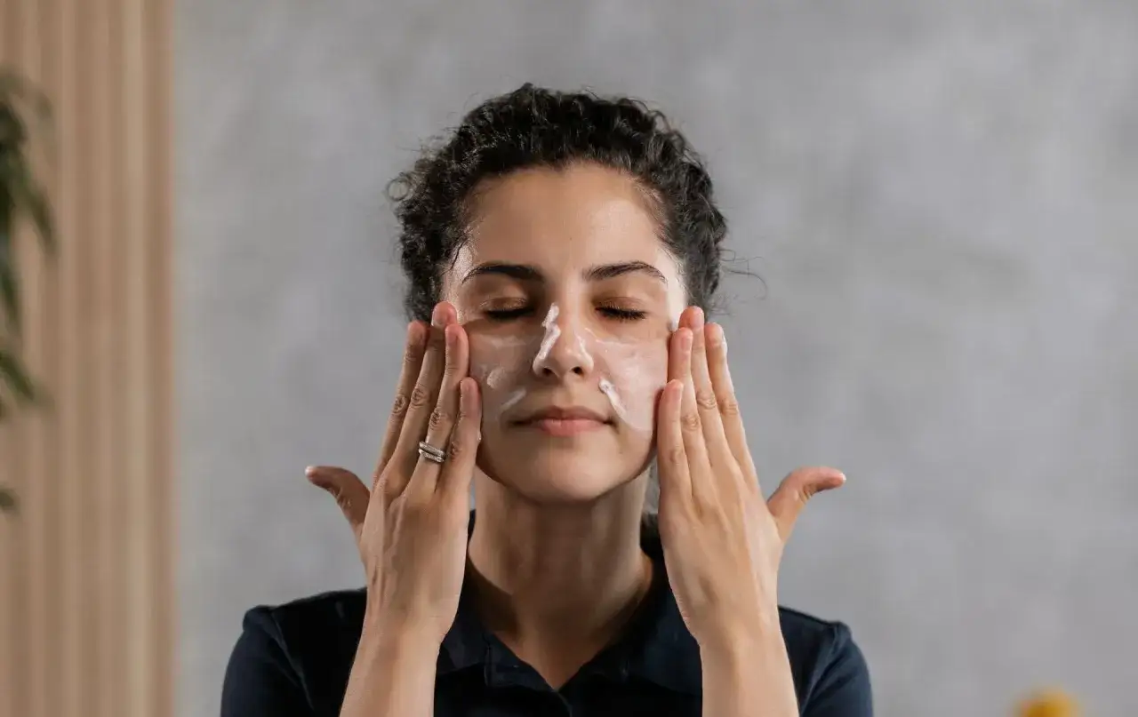 Donna con gli occhi chiusi applica una crema sul viso, un gesto di cura per la pelle naturale.