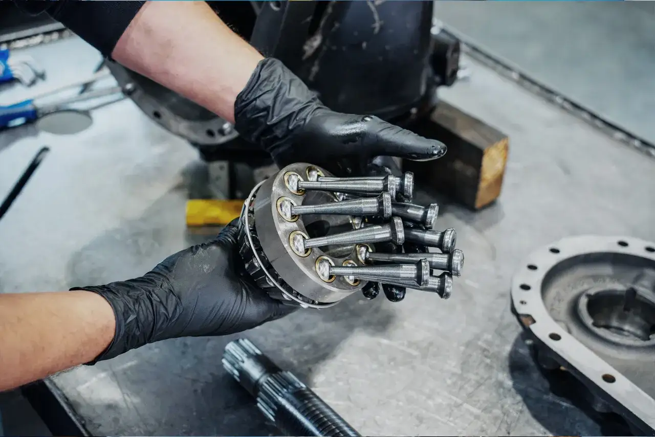 Mechanik w czarnych rękawiczkach trzyma element silnika. Brak kompresji na cylindrze może oznaczać wysoki koszt naprawy.