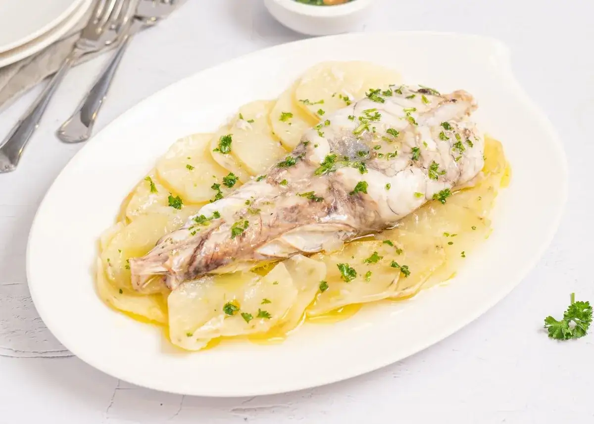 Delicioso rape al horno sobre patatas laminadas, espolvoreado con perejil fresco. Un plato principal sencillo y sabroso.