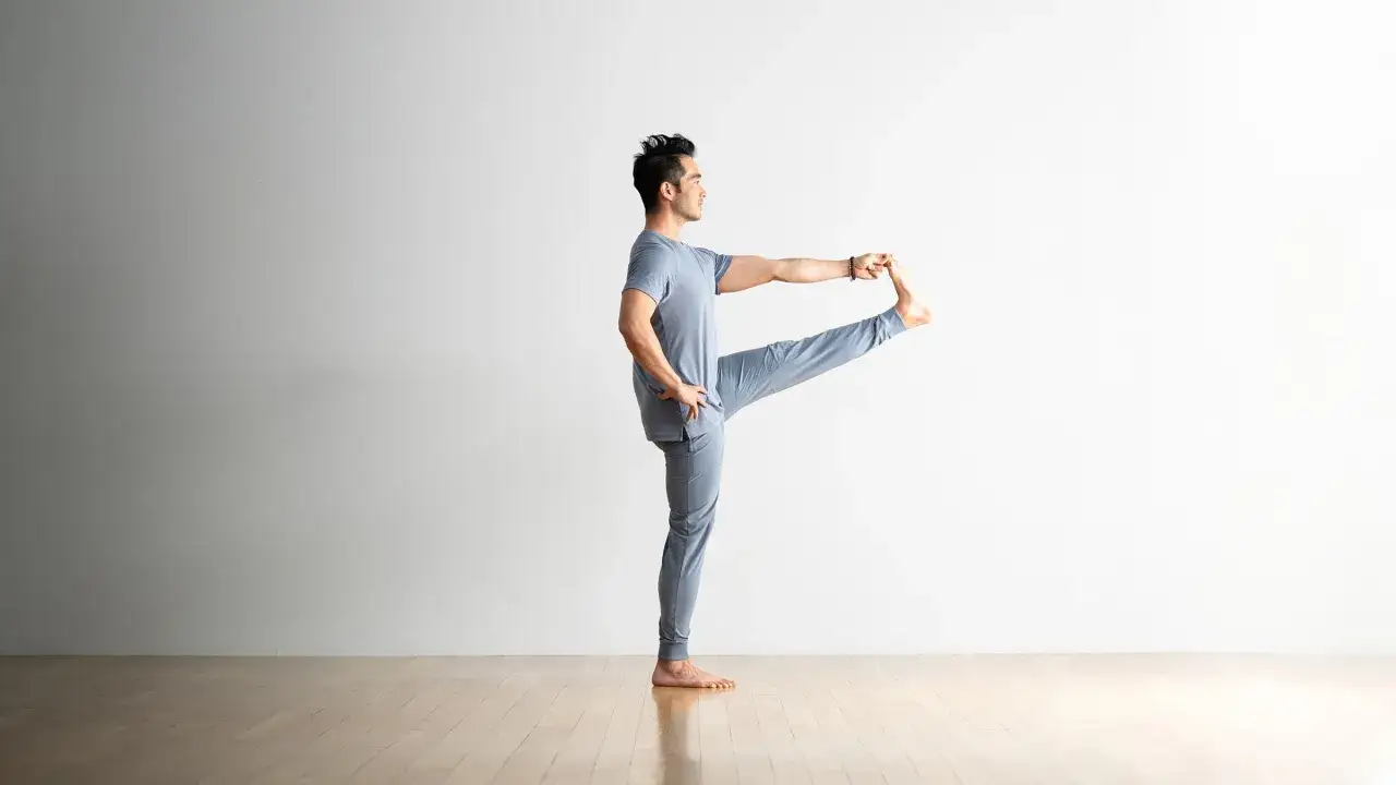 Mężczyzna w pozycji utthita hasta padangusthasana, z uniesioną i chwytaną stopą, ćwiczy r&oacute;wnowagę.